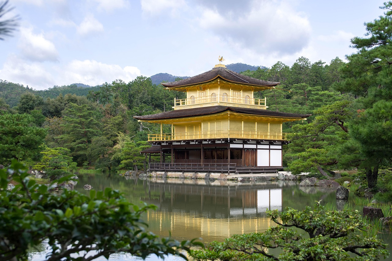 A golden pavilion reflected in a calm pond surrounded by lush greenery.