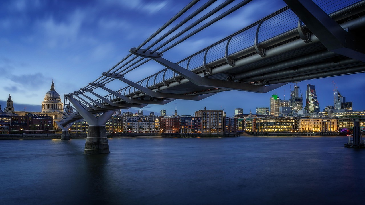 A view of a modern bridge over a river at dusk with a city skyline in the background.