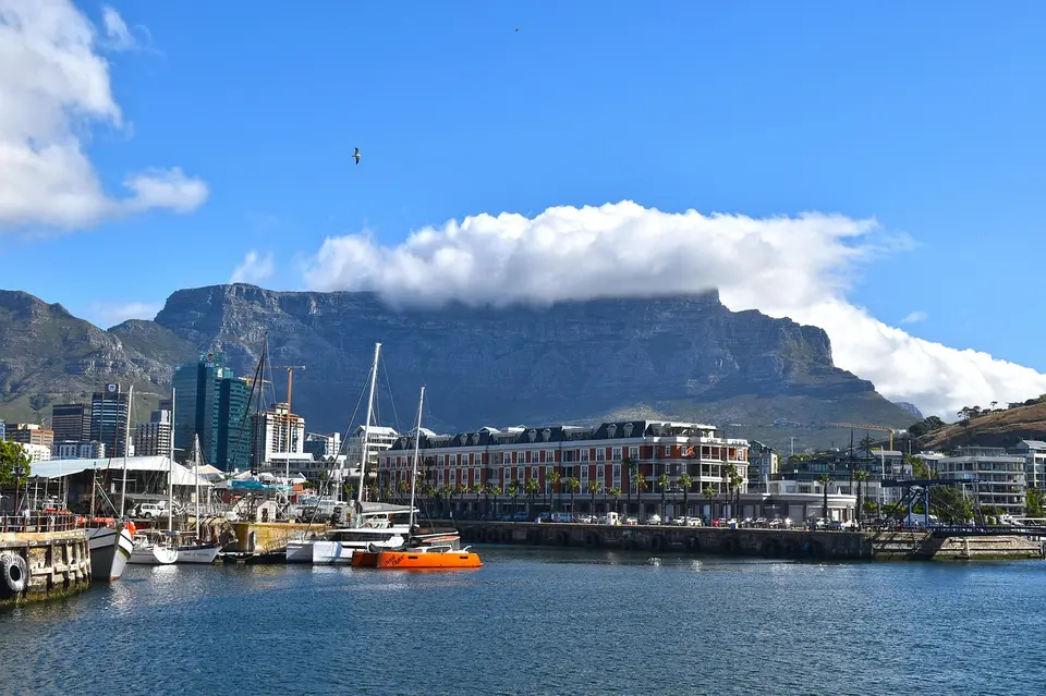 A scenic view of a harbor with boats, buildings, and a prominent mountain in the background under a clear blue sky.