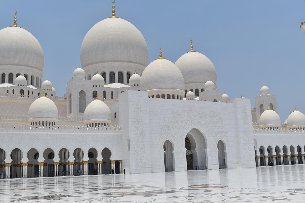 A grand mosque with multiple white domes and arches reflected in a calm pool of water.