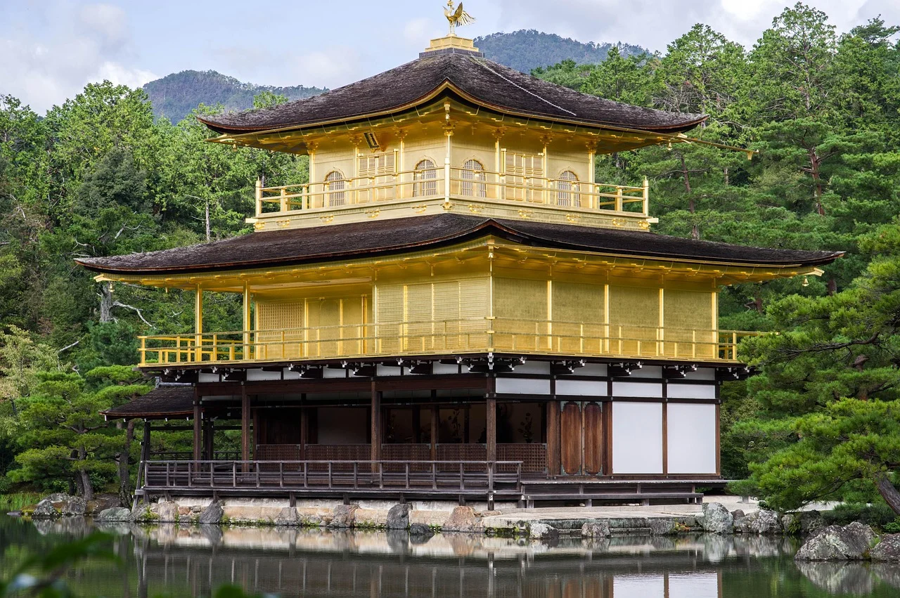 A golden pavilion with traditional Japanese architecture surrounded by a serene landscape with trees and a reflective pond.