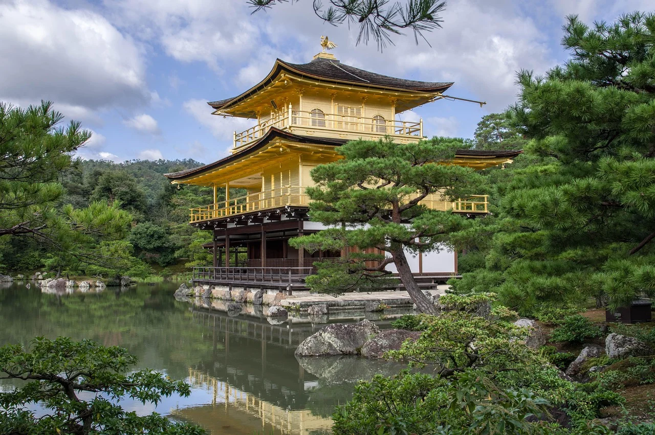 A golden pavilion reflecting in a calm pond surrounded by lush greenery.