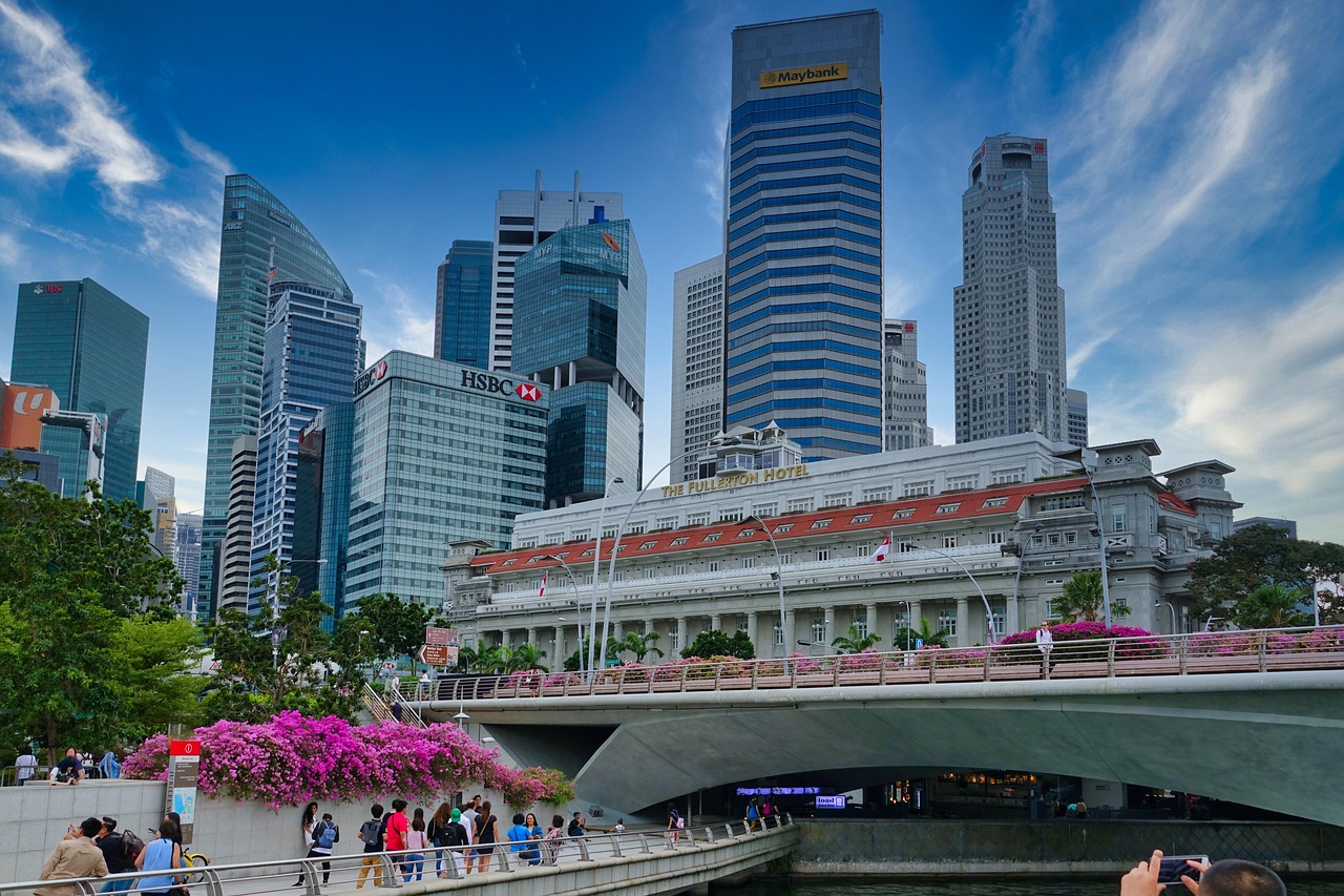 A bustling cityscape with tall skyscrapers, a bridge with pink flowers, and the Fullerton Hotel in the foreground.