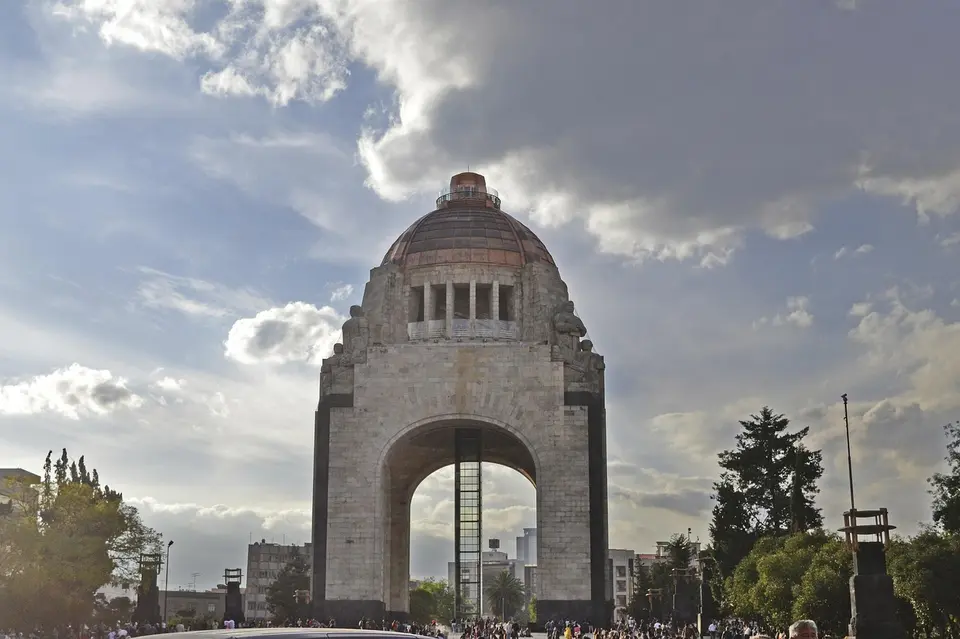 A large stone arch monument with a dome on top, under a partly cloudy sky, with people gathered around it.