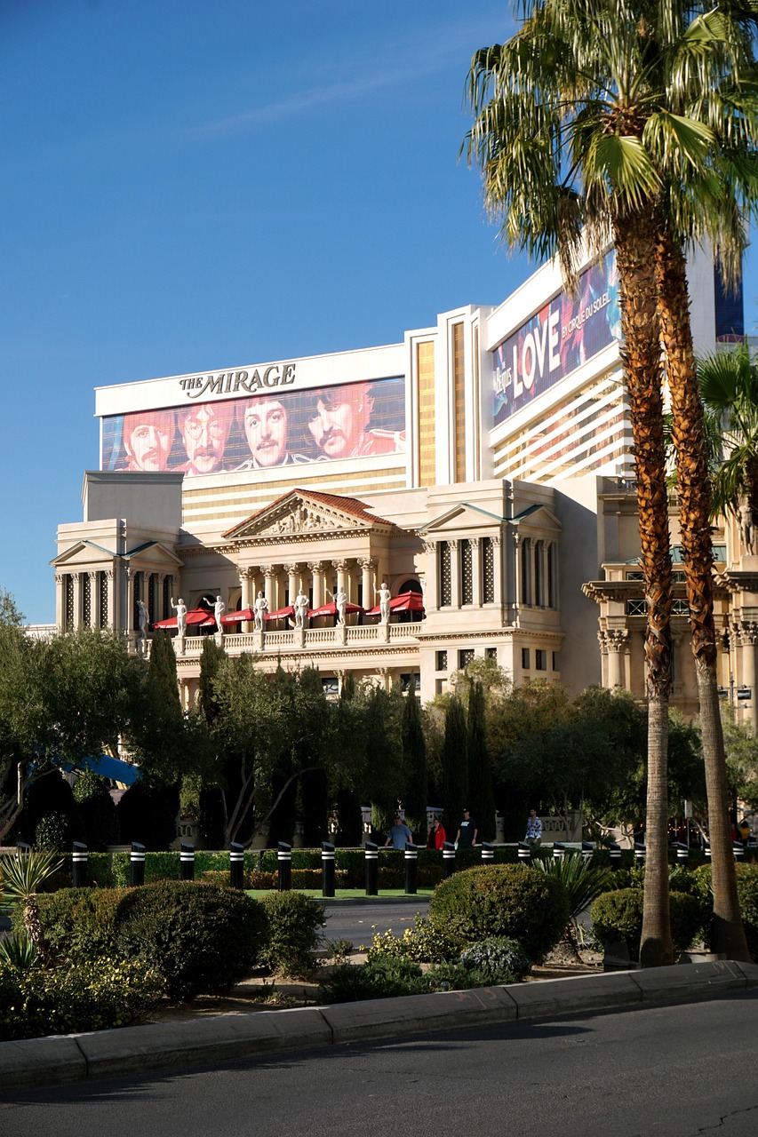 The exterior of The Mirage hotel and casino in Las Vegas with palm trees and billboards.