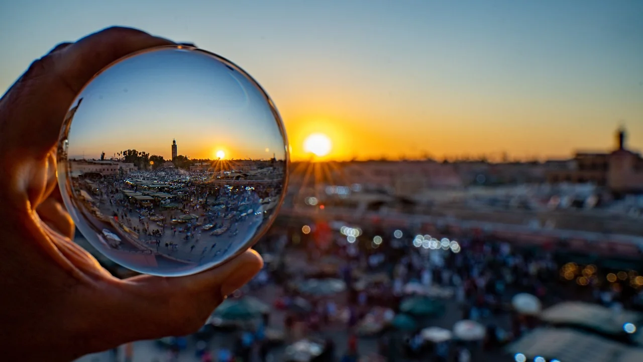 A hand holding a crystal ball reflecting the sunset over a bustling city market with a recognizable landmark in the distance.