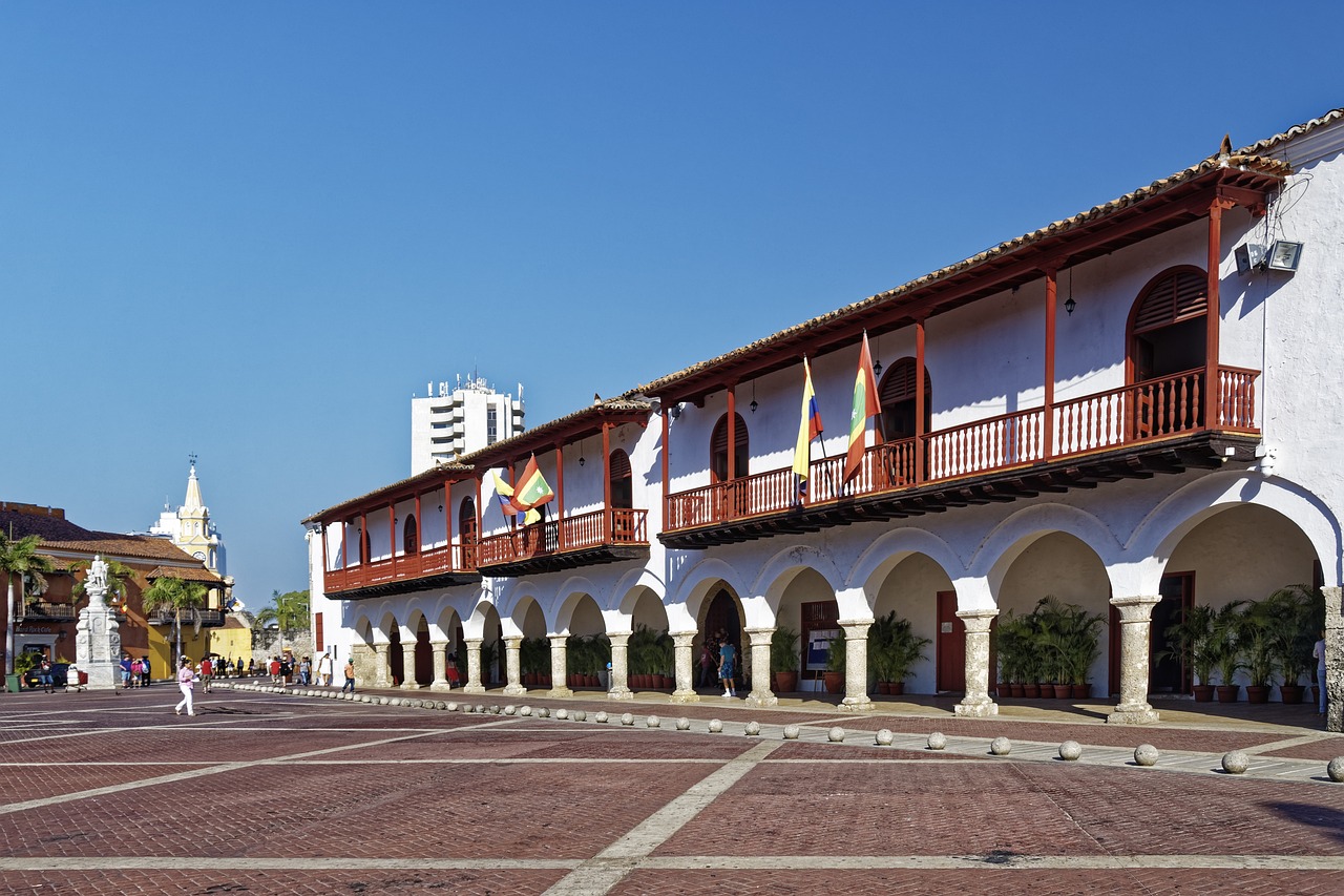A historic building with arches and a balcony in a public square with people walking around.