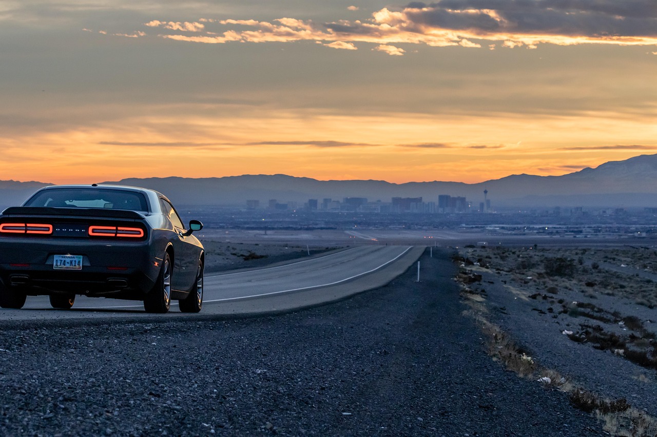 A car on a road at sunset with a city skyline in the distance and mountains in the background.
