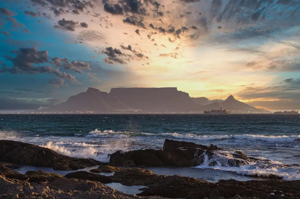 A scenic view of Table Mountain at sunset over the ocean in Cape Town, South Africa.