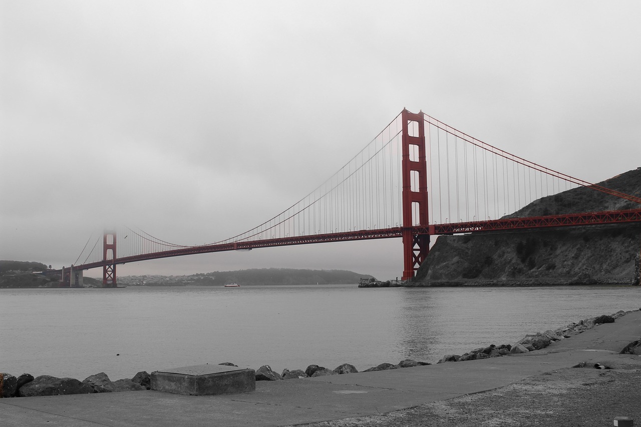 A foggy view of the Golden Gate Bridge spanning across a body of water with a rocky shoreline in the foreground.