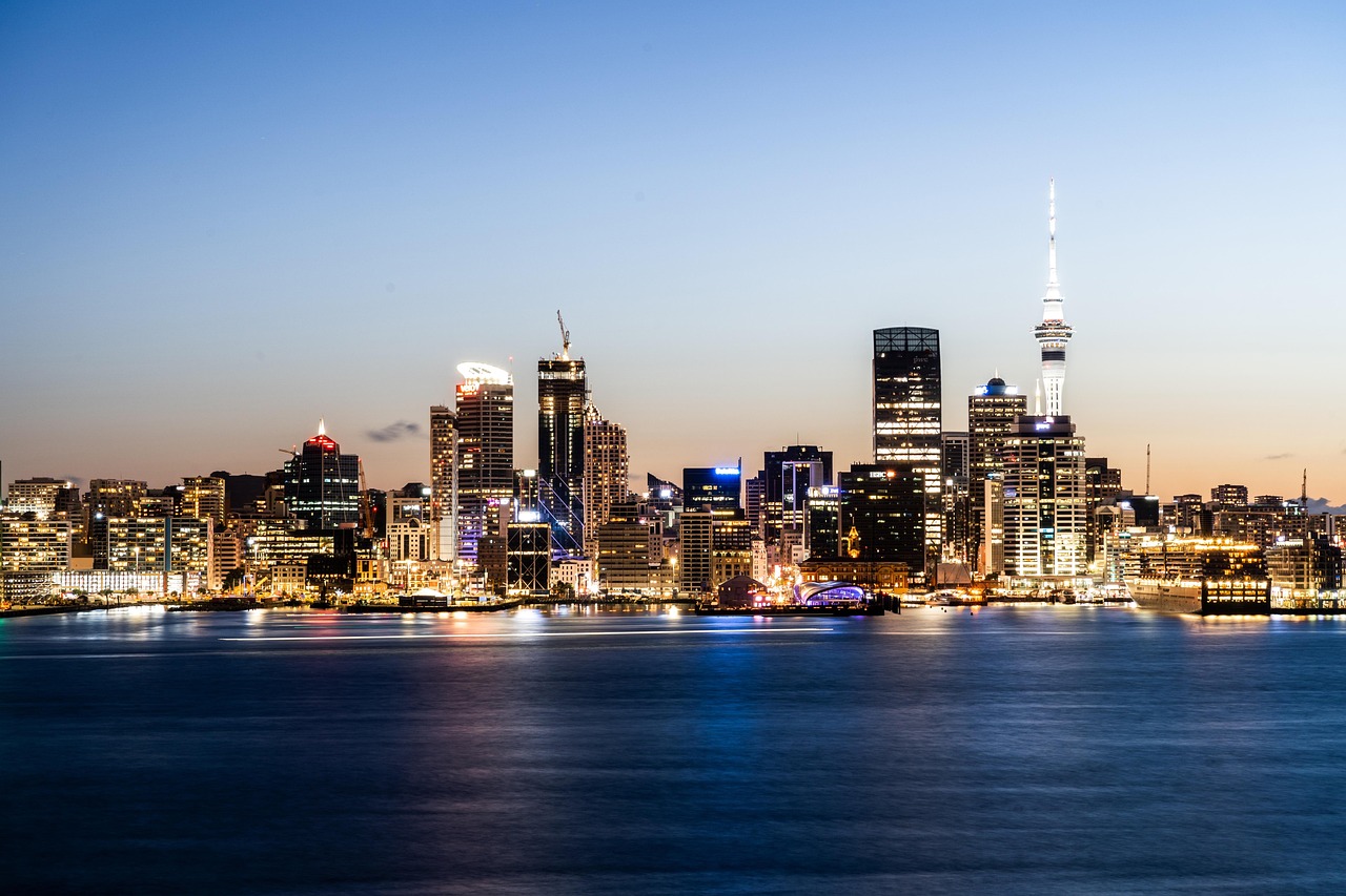 Nighttime cityscape of Auckland with illuminated skyscrapers and a calm waterfront.
