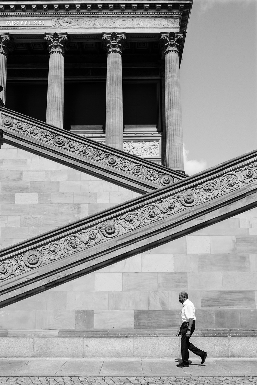 A man walking in front of a grand neoclassical building with large columns and ornate staircases.