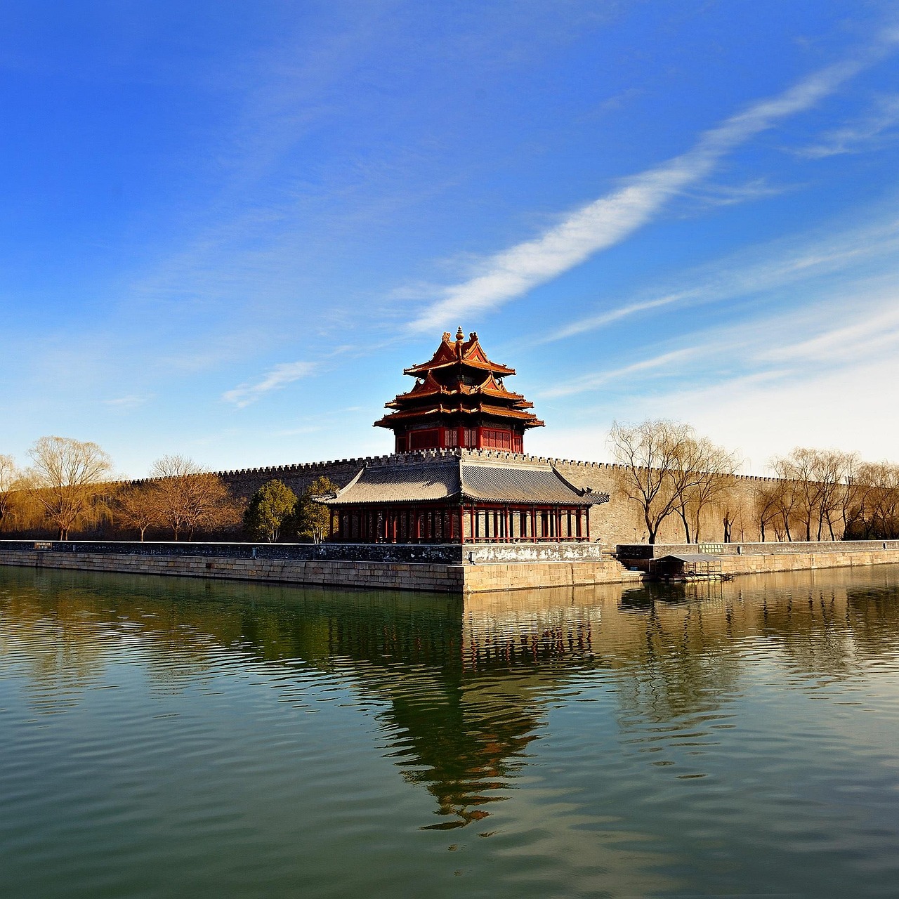 A traditional Chinese building with a red roof and ornate details reflected in a calm body of water, with a clear blue sky above.