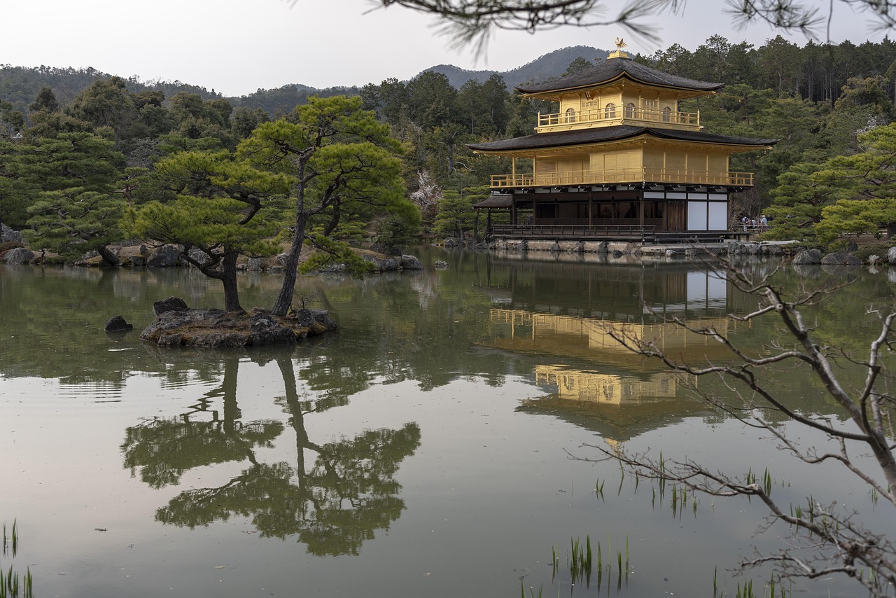 A golden pavilion reflected in a calm pond surrounded by trees and rocks.