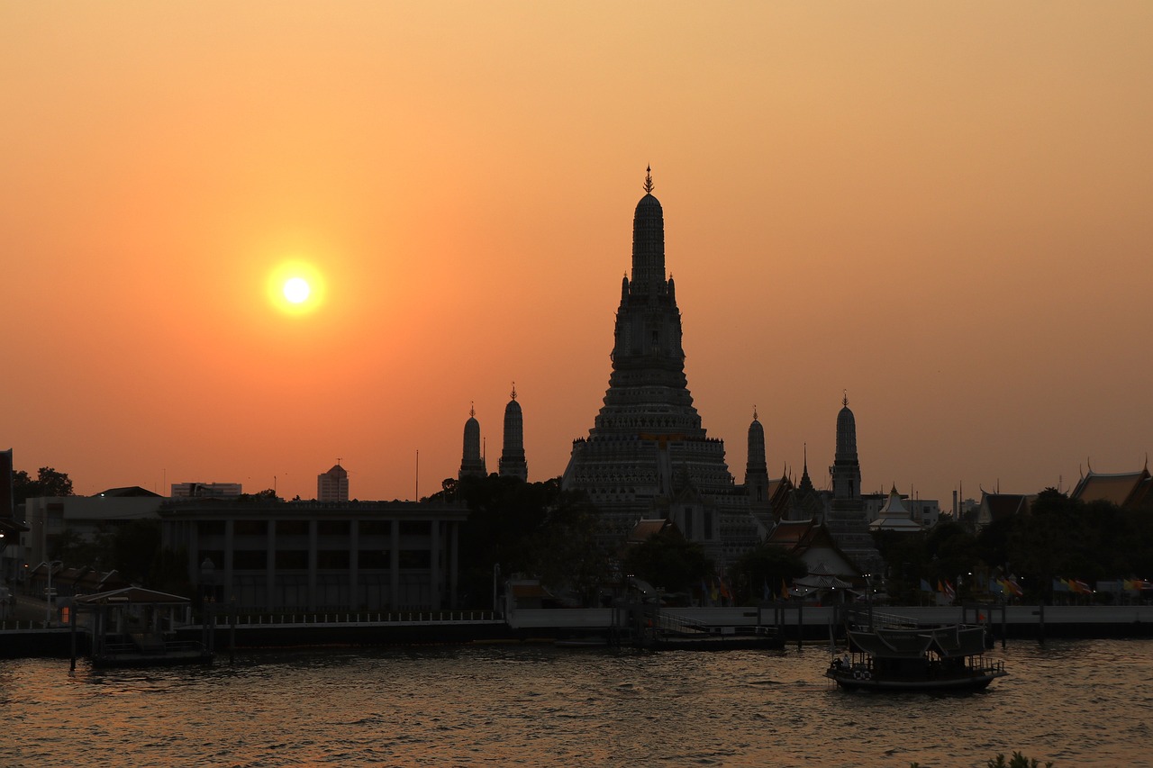A sunset view of a temple complex with a river in the foreground and a boat.