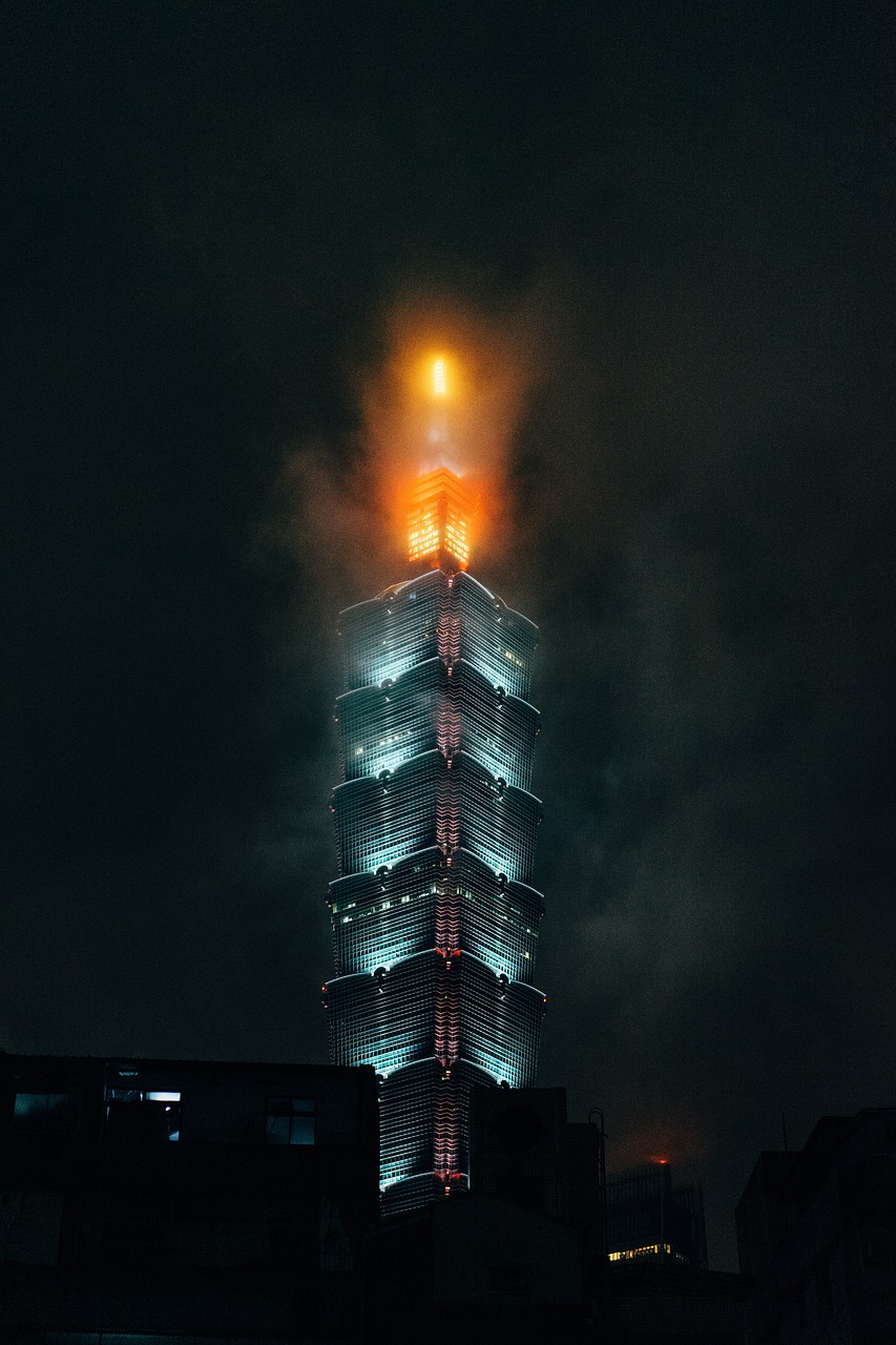 A tall skyscraper illuminated at night with a bright light at the top.