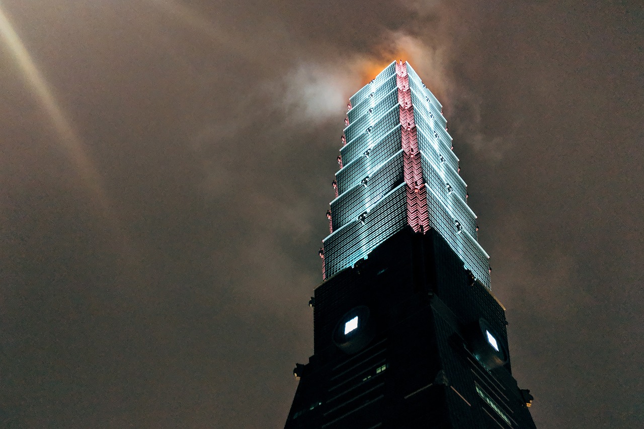 A tall skyscraper with smoke coming from the top at night.