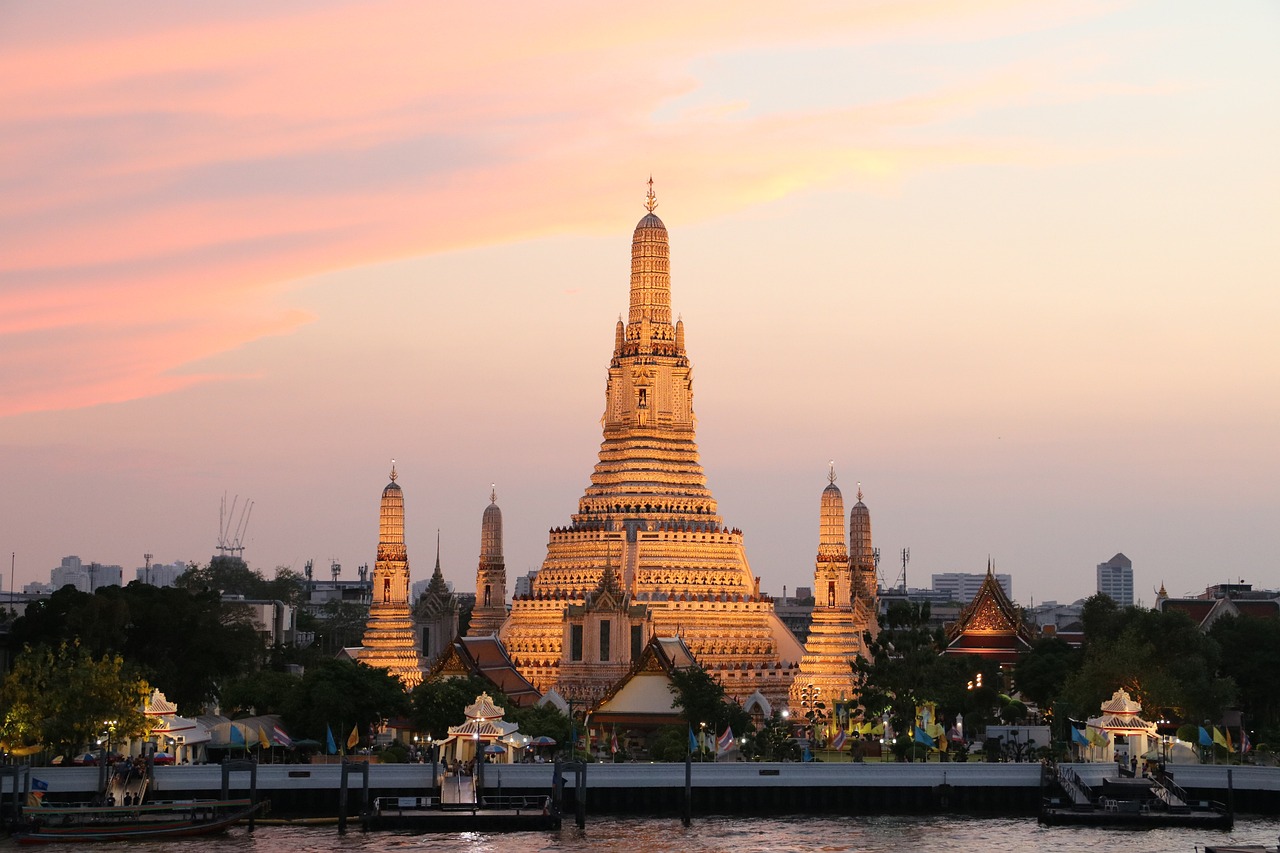 A golden temple complex at sunset with a river in the foreground and city skyline in the background.