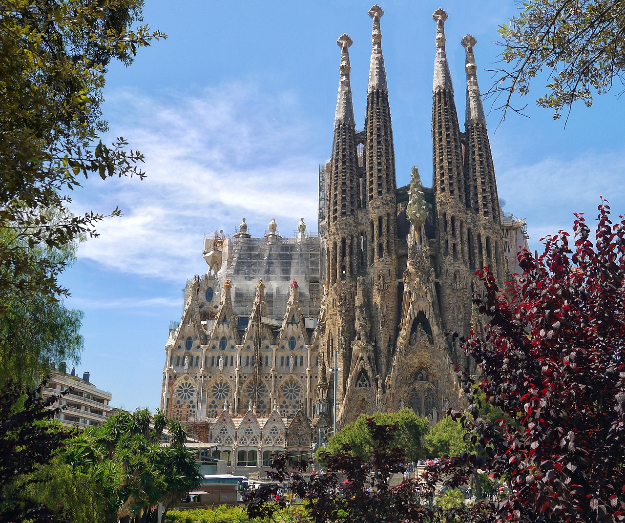 The Sagrada Familia, a large and intricate basilica in Barcelona, Spain, with tall spires and detailed stonework, surrounded by greenery.