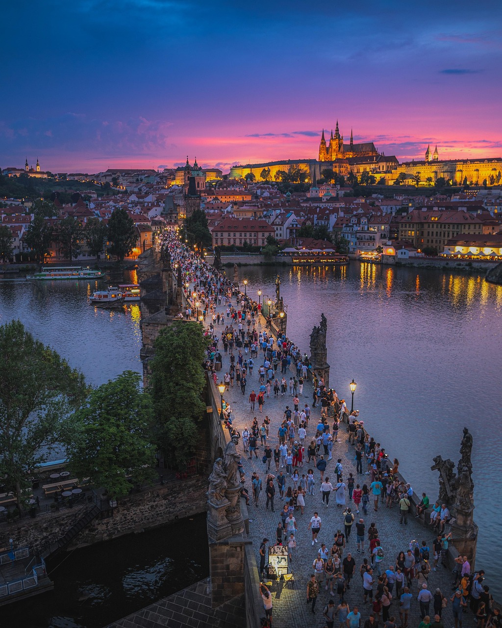 A bustling bridge over a river at dusk with a cityscape in the background.