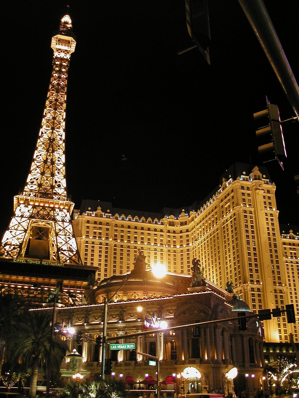 Night view of the Paris Las Vegas hotel and casino with an illuminated Eiffel Tower replica and a busy street in front.