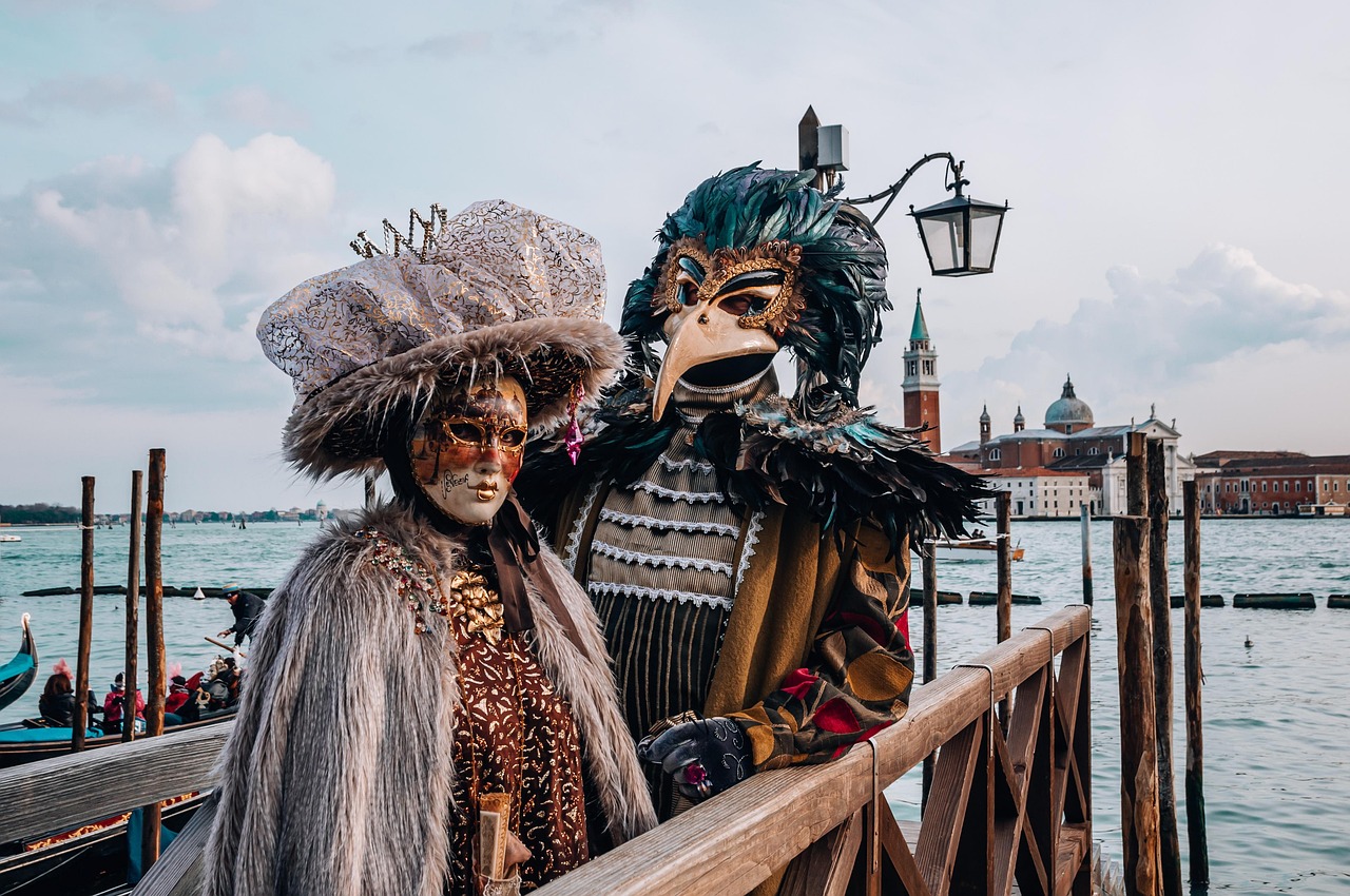 Two people in elaborate carnival costumes standing by a waterfront in Venice, Italy.
