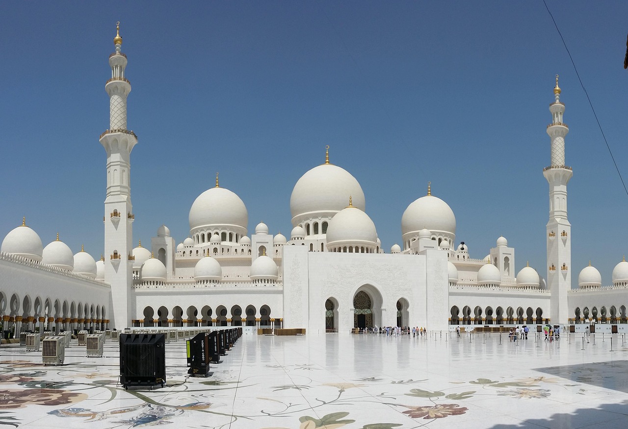 A grand mosque with multiple white domes and tall minarets under a clear blue sky.