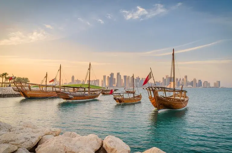 Traditional boats on the water with a city skyline in the background at sunset.
