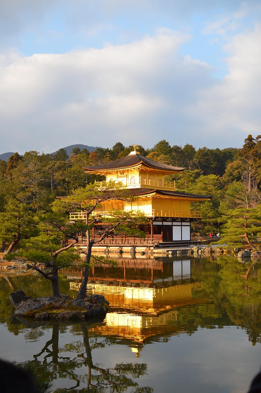 A golden pavilion reflected in a calm pond surrounded by trees and greenery.