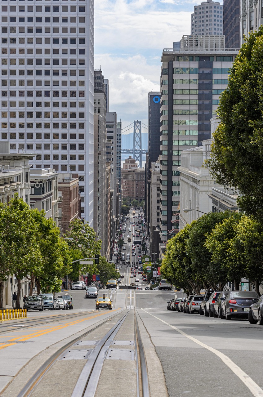 A busy urban street in San Francisco with tall buildings, traffic, and a cable car track.