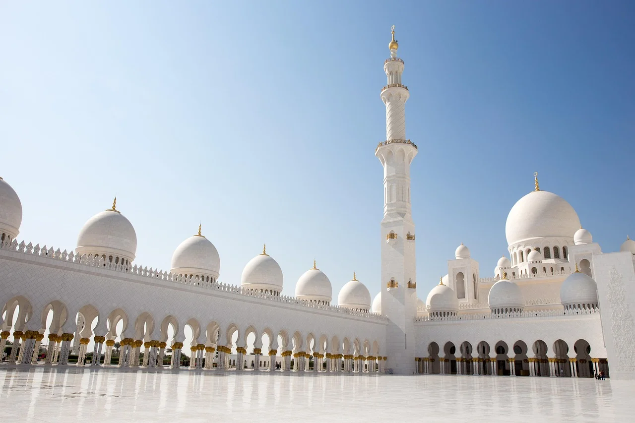 A grand white mosque with multiple domes and a tall minaret under a clear blue sky.