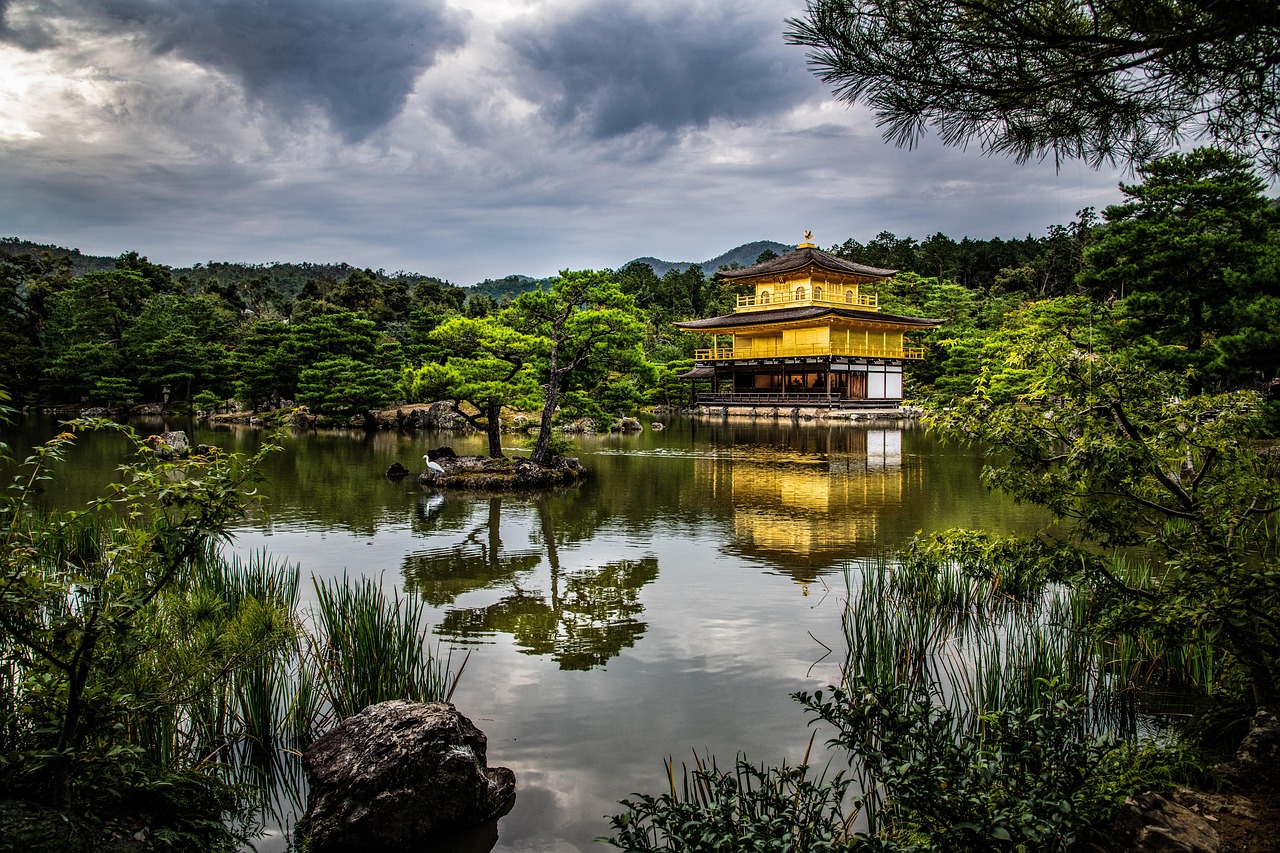 A golden pavilion reflected in a calm pond surrounded by lush greenery and trees.