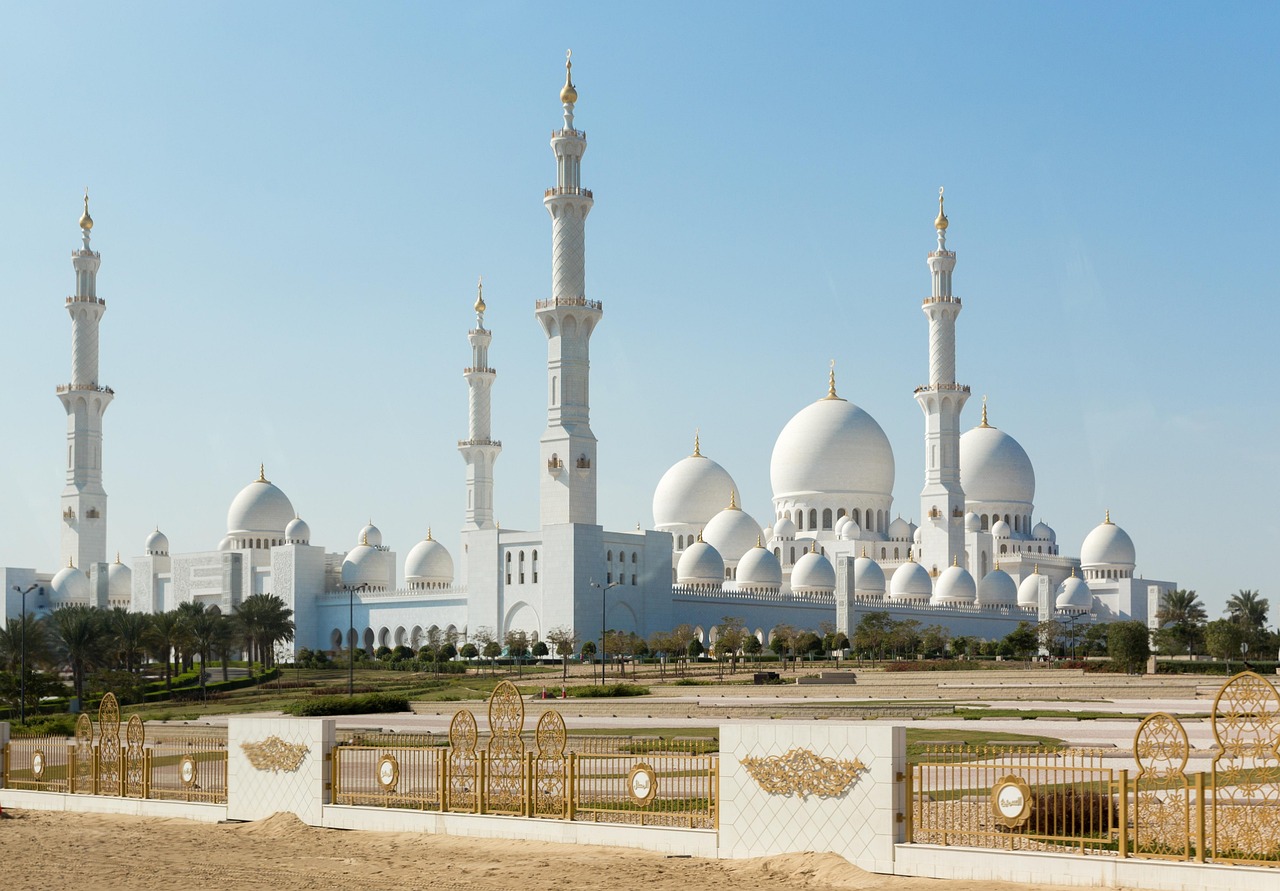 A grand mosque with multiple white domes and tall minarets under a clear blue sky.