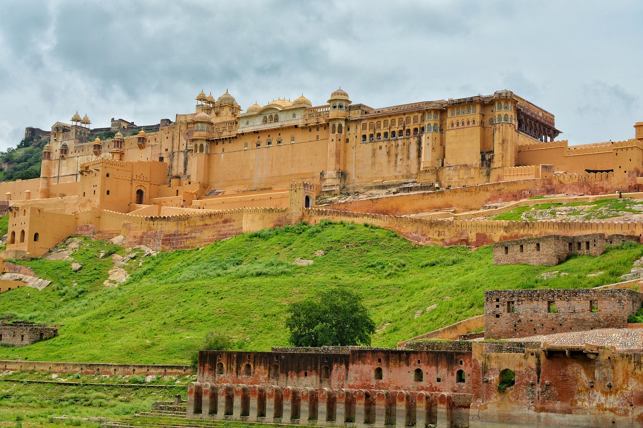 A large, historic fort with yellow walls and multiple domed structures, situated on a hill with green grass and stone pathways.