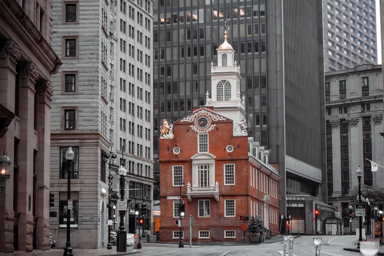 A historic red brick building with a clock tower surrounded by modern skyscrapers in an urban setting.
