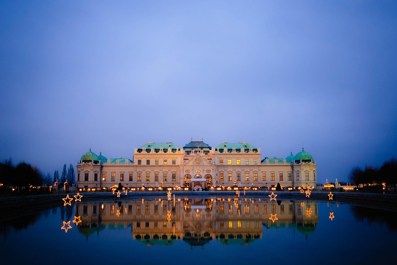 A grand palace illuminated at night, reflected in a calm body of water with star-shaped lights in the foreground.