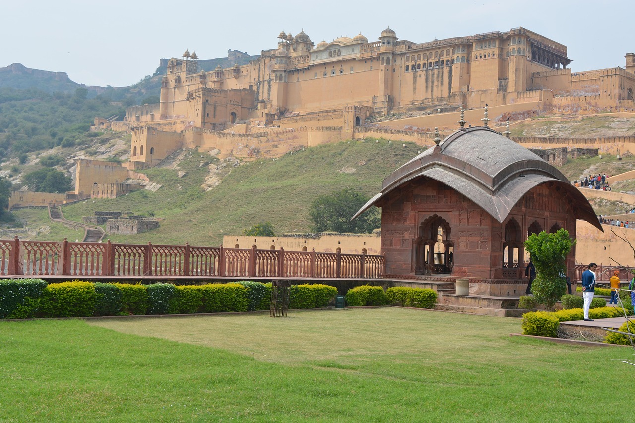 A large historical fort on a hill with a smaller pavilion in the foreground and well-maintained gardens.