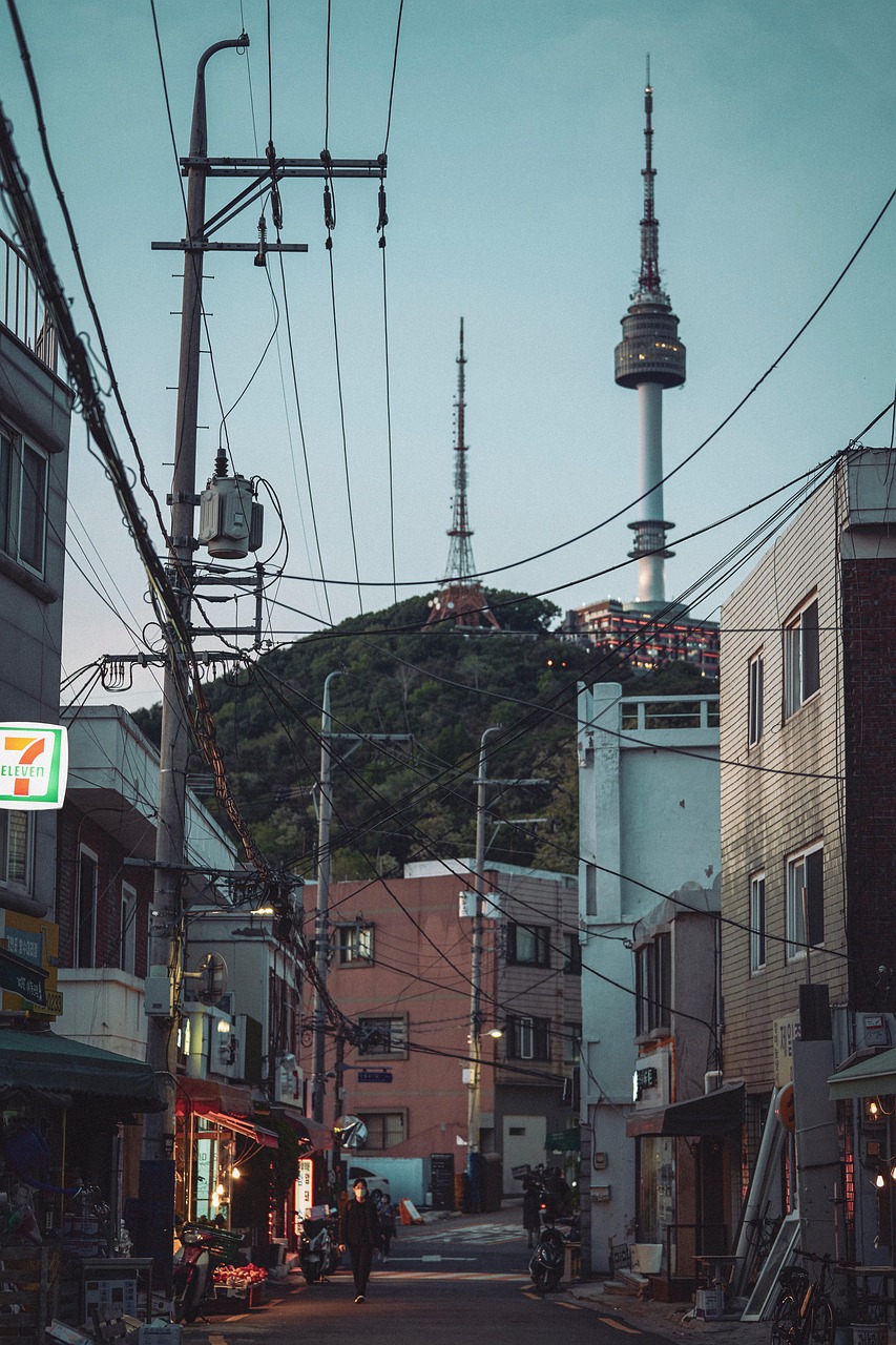 A narrow street in Seoul with power lines and buildings, featuring the N Seoul Tower in the background.