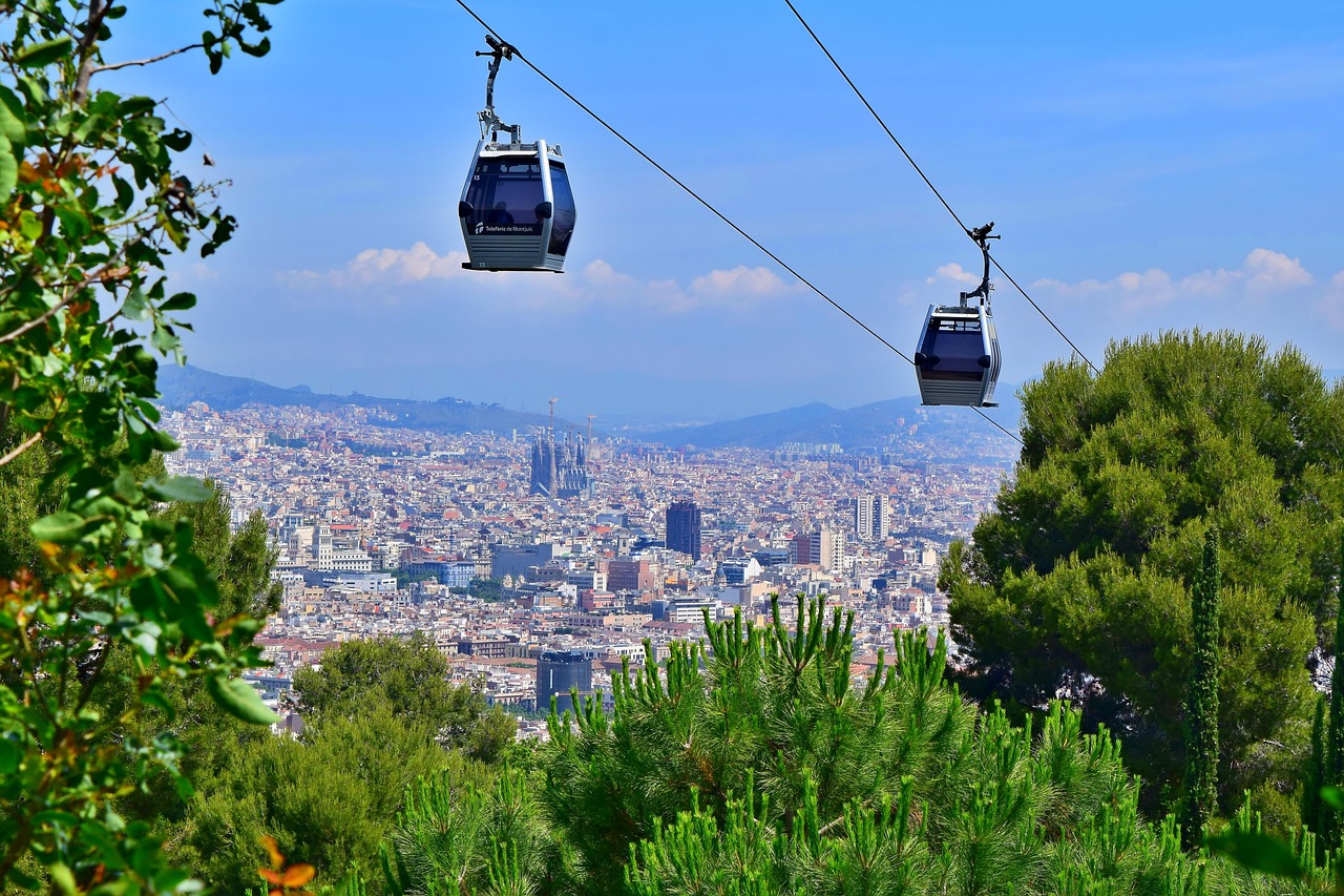 A panoramic view of a city with cable cars in the foreground and a dense urban landscape in the background, surrounded by greenery.
