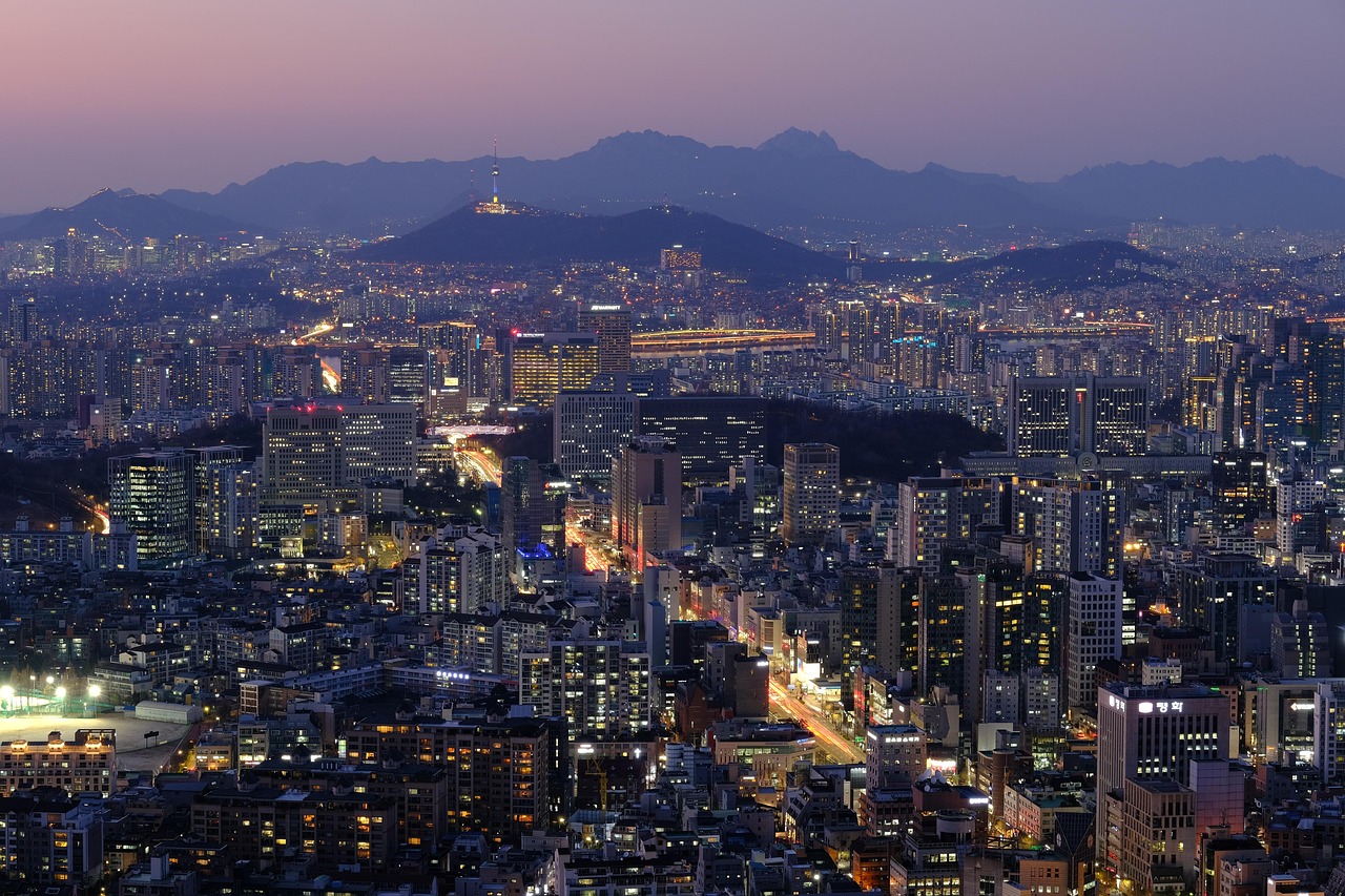 Nighttime cityscape of a densely populated urban area with illuminated buildings and mountains in the background.