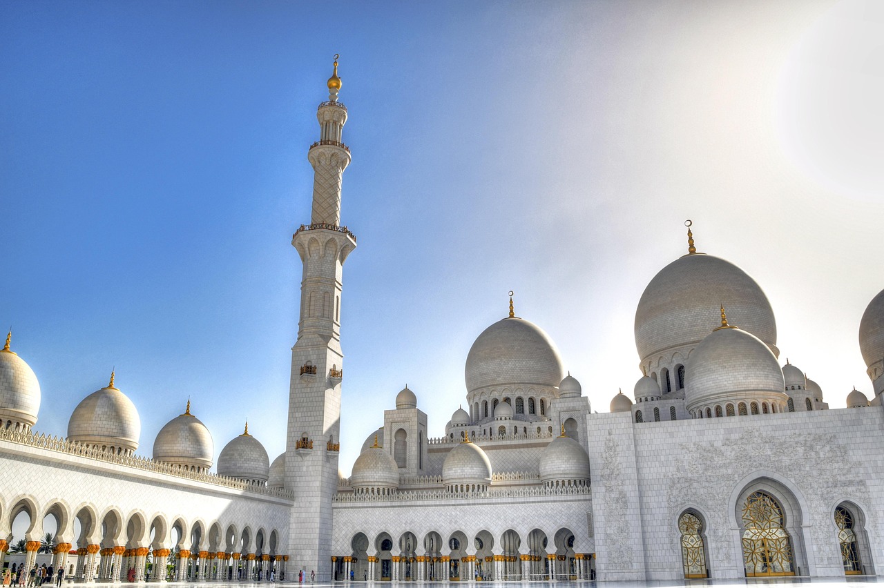 A grand white mosque with multiple domes and a tall minaret under a clear blue sky.