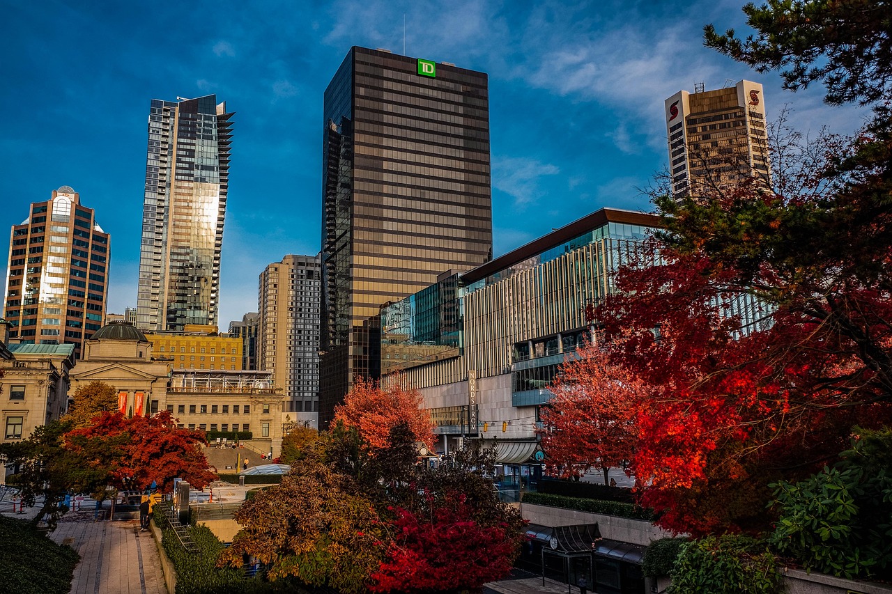 A cityscape with tall buildings and trees with red and orange leaves in the foreground.