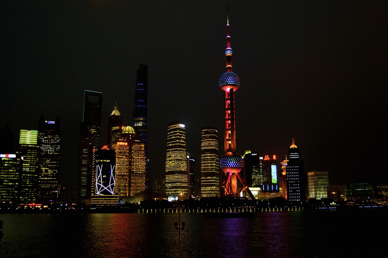 Night view of a city skyline with illuminated skyscrapers and a prominent tower by the waterfront.