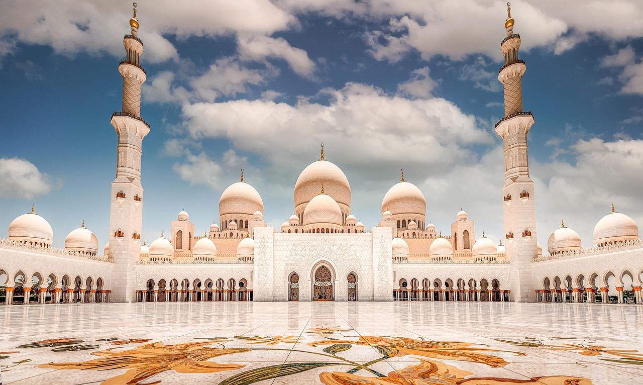A grand mosque with multiple domes and minarets under a blue sky with clouds.