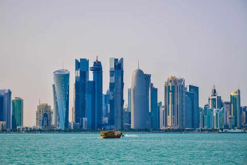 A city skyline with modern buildings along a waterfront, featuring a boat in the foreground.