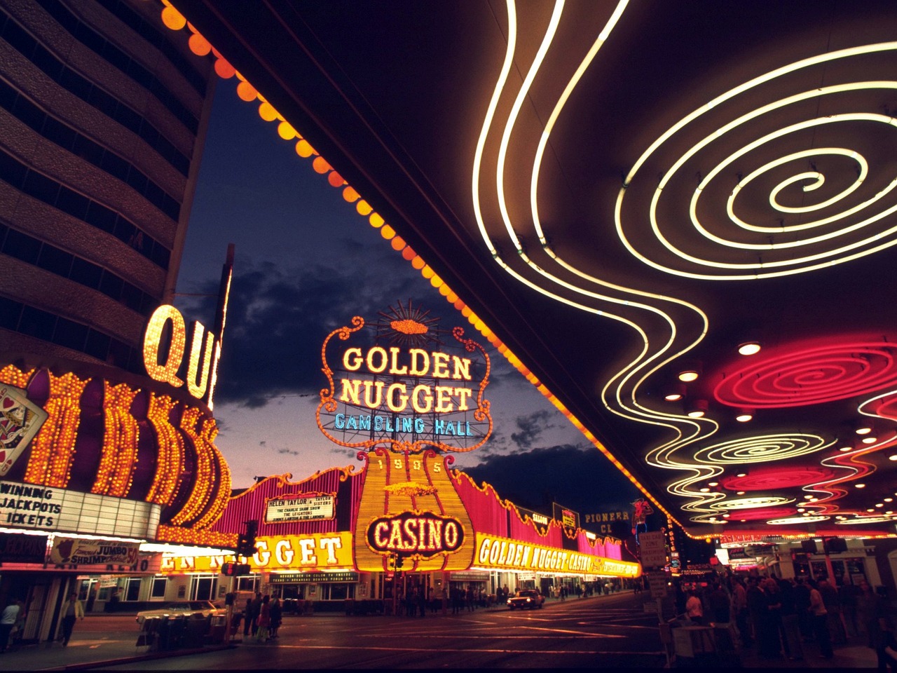 A night view of a bustling street in Las Vegas with bright neon signs of casinos, including the Golden Nugget.