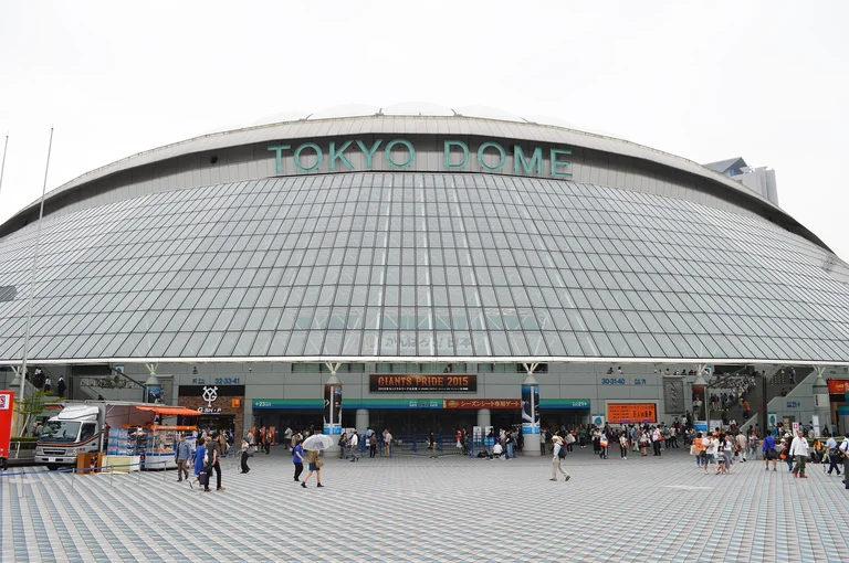 A large crowd of people gathered in front of the Tokyo Dome stadium entrance on a cloudy day.