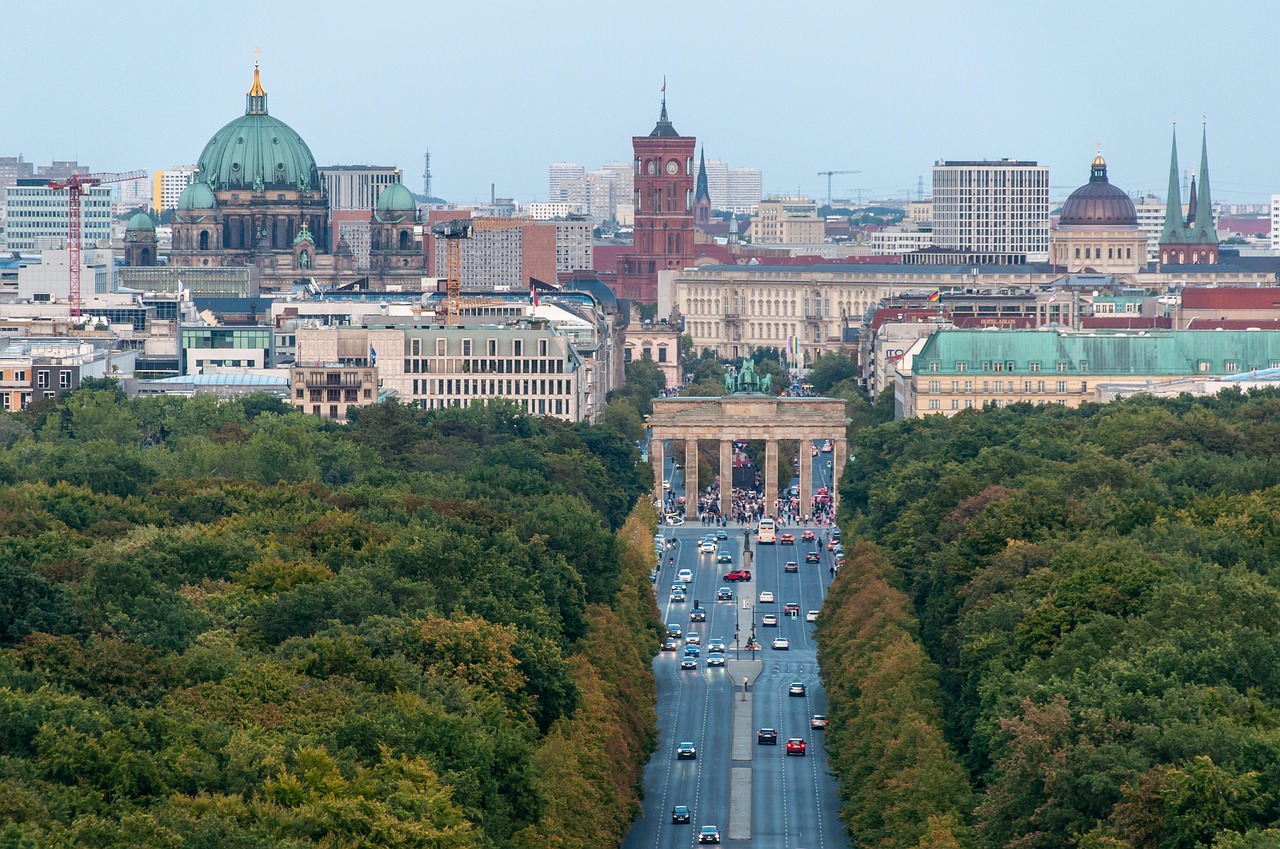 Aerial view of a city with a prominent archway, trees lining a busy street, and historic buildings in the background.