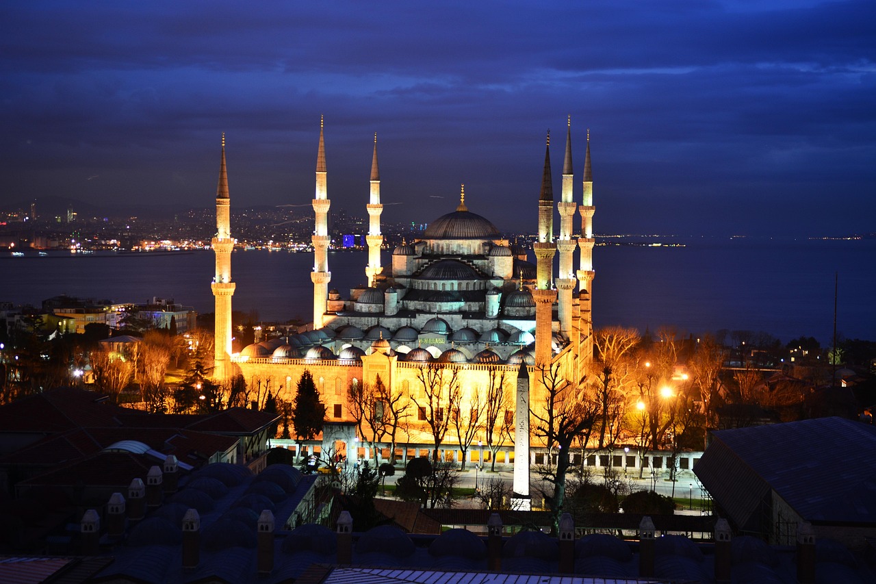 A night view of the Blue Mosque in Istanbul, Turkey, with the city lights reflecting on the water.