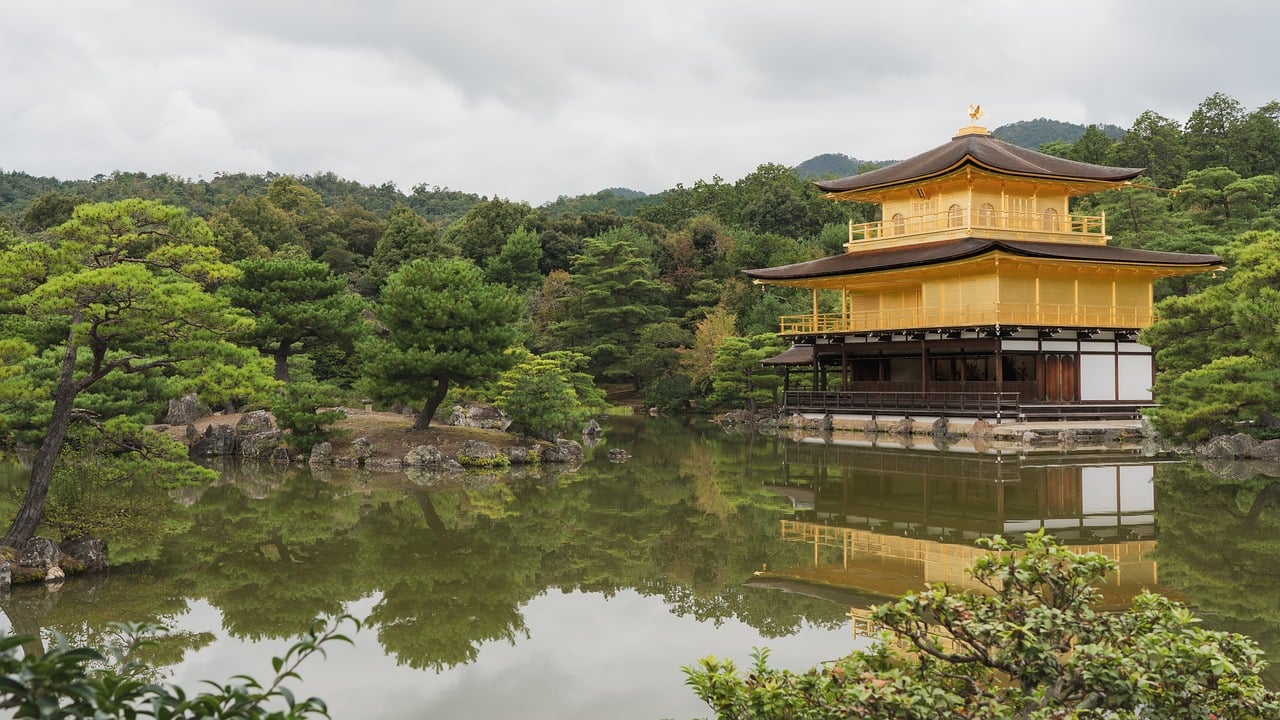 A golden pavilion reflected in a calm pond surrounded by lush greenery.